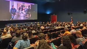 Foto dos participantes do evento no Cine Metrópolis. Na tela, a imagem do secretário de Educação Superior, que participou de forma remota.
