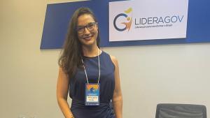 Foto da servidora posando ao lado de uma placa com a logomarca do evento