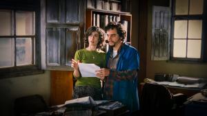Cena do filme Saneamento Básico, na qual dois personagens (uma mulher e um homem) estão em um escritório, segurando um papel nas mãos