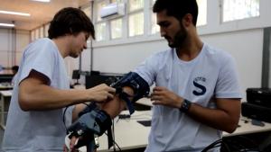 Foto de dois rapazes testando um braço mecânico desenvolvido dentro do Espaço